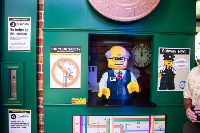 A Lego sculpture of an MTA employee in an old-fashioned token booth clerk, with the old NYC subway toekn above. There's also a sign that says the J is not working and a subway map of midtown.